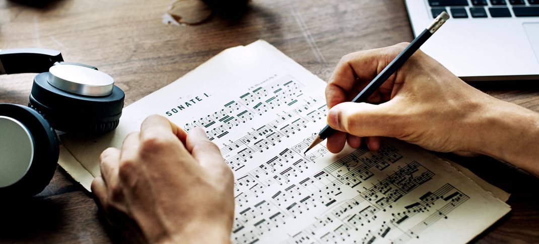 Een hand die met een potlood aantekeningen maakt aan de noten op een muziekblad.