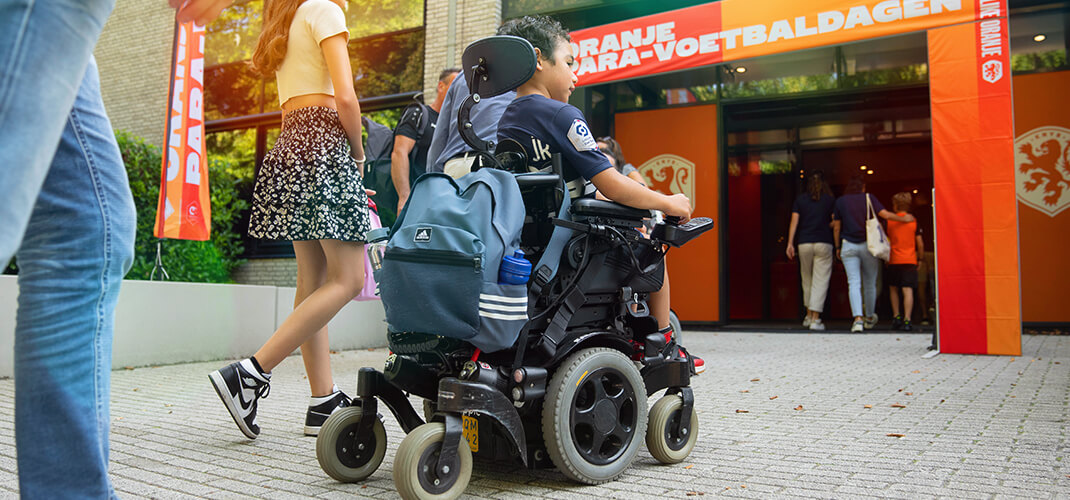 Jongen met elektrische rolstoel voor de ingang van de Oranje Para-voetbaldagen.