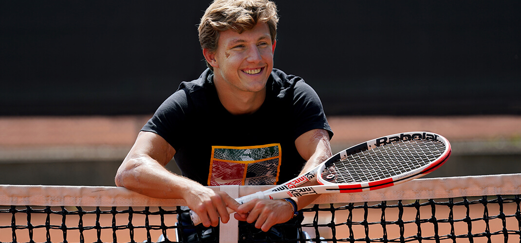 Niels die op het tennisnet hangt met zijn tennisracket..